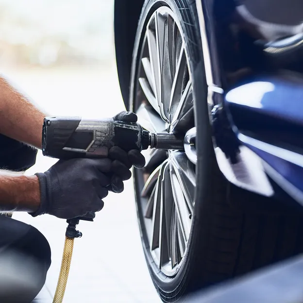 Mécanicien nettoyant une roue de voiture avec un appareil haute pression.