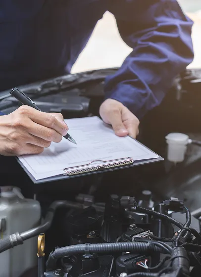 Mécanicien Peugeot notant contrôle technique sous capot de voiture.